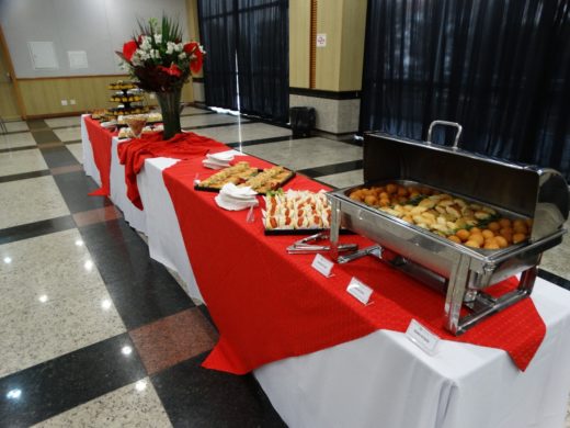 Estrutura longa de buffet corporativo com rechauds, salgados e lanches montada em salão de eventos.
