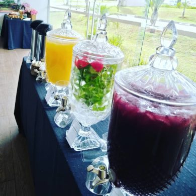 Salão decorado para evento social com mesas prontas, arranjos florais e iluminação aconchegante.